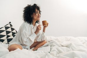 shutterstock 2107015442 295x197 - Young,Mixed,Race,Woman,Sitting,On,Bed,Having,Coffee,And