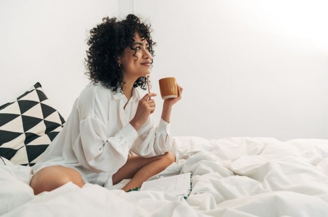 Young,Mixed,Race,Woman,Sitting,On,Bed,Having,Coffee,And